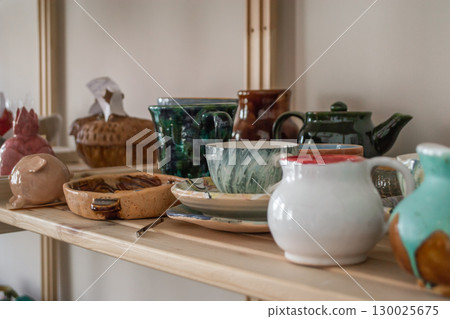 ceramic craft variety handmade pottery on wooden shelves in cozy workshop setting. closeup. ceramic craft variety handmade pottery on wooden shelves in cozy workshop setting. closeup. 130025675