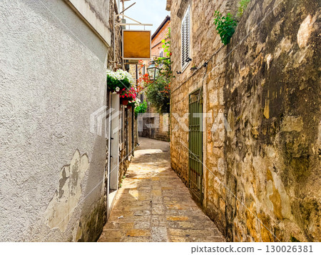 Sunny alley with stone walls and hanging flowers. Urban atmosphere and cultural heritage of Mediterranean historic streets. 130026381