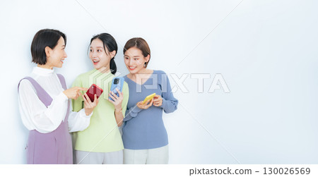 A group of middle-aged women talking while looking at their smartphones 130026569