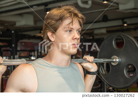 Bodybuilder and sporty young man exercising with barbell at fitness center. Cross training. Male athlete lifting weights. 130027262