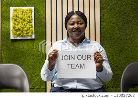 African american HR manager holds office ad that welcomes applicants to apply for job openings, encouraging career development and workforce growth through hiring message advertisement. 130027268