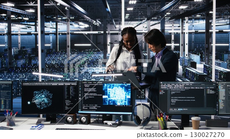 Team of data center engineers looking over paperwork and using deep learning algorithms to analyze datasets. Employees in multiethnic server farm using AI to recognize data patterns, camera A Team of data center engineers looking over paperwork and using deep learning algorithms to analyze datasets. Employees in multiethnic server farm using AI to recognize data patterns, camera A 130027270