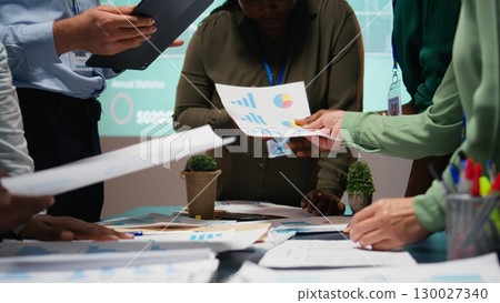 Business colleagues attending in a late night briefing session for teamwork, exchanging documents and reviewing finance updates. Aligning objectives through problem solving. Camera A. 130027340