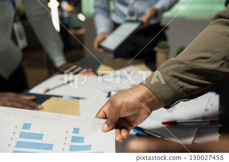 Close up of diverse project team shares analytics reports during advisory board event after hours, reviewing business intel and preparing insight for upcoming presentation with associates. 130027458