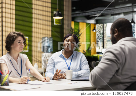 Black job seeker sitting across from human resources team during hiring process discussion, presenting his work experience and qualifications for the business organization job offer. Career goals. Black job seeker sitting across from human resources team during hiring process discussion, presenting his work experience and qualifications for the business organization job offer. Career goals. 130027473