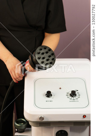 Beautician holding cavitation handpiece near machine control unit. Beautician holding cavitation handpiece near machine control unit. 130027792