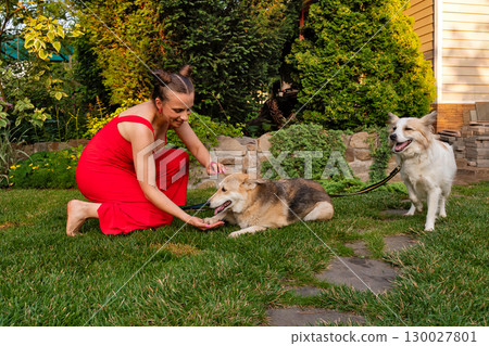 Woman kneeling petting two dogs in lush garden setting 130027801