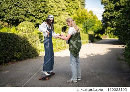 Young women enjoying a sunny afternoon skateboarding in a lush park 130028105