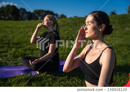 Two women practicing mindfulness in a serene green park under blue skies 130028120