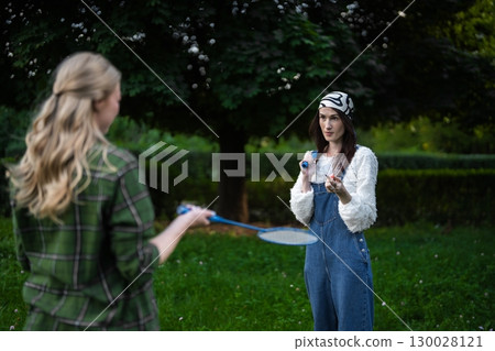 Two friends enjoying a playful badminton match in a lush green park 130028121