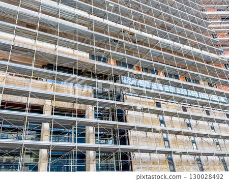 Facade of tall building covered in scaffolding. Symbol of engineering, progress and structural development in urban space 130028492