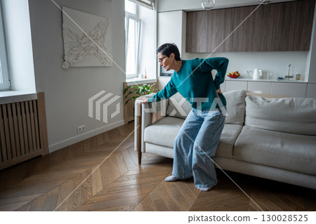 Elderly woman bent with agony try to get up from couch due to spinal problem. Disc herniation Elderly woman bent with agony try to get up from couch due to spinal problem. Disc herniation 130028525