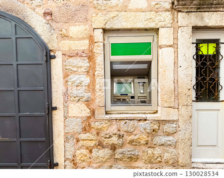 ATM machine installed in a stone building wall with visible access panel. Finance, banking service and secure urban technology system. ATM machine installed in a stone building wall with visible access panel. Finance, banking service and secure urban technology system. 130028534
