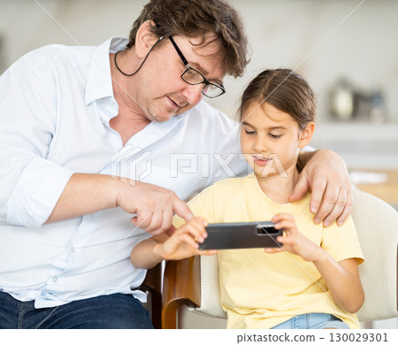 Daughter shows something to father on phone 130029301