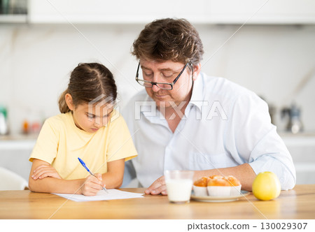 Father helping little daughter do school homework in kitchen 130029307