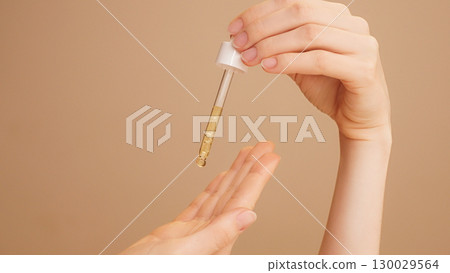 Close-up of female hands on isolated beige background holding dropper, anti-aging facial serum, booster dripping on palm.Commercial skincare, moisturizing, vitamin c, anti-wrinkle products advertising Close-up of female hands on isolated beige background holding dropper, anti-aging facial serum, booster dripping on palm.Commercial skincare, moisturizing, vitamin c, anti-wrinkle products advertising 130029564