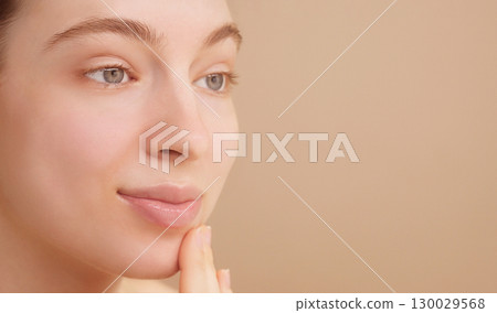 Close-up portrait happy attractive young woman apply facial oil serum or moisturizer. The concept of skincare advertising, beauty routine. Young girl's face on a light studio background. Copy space 130029568