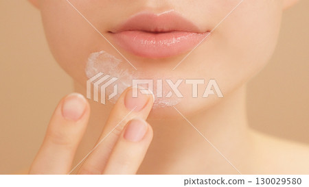 Half face portrait. Close-up of a young woman gently applies acne cream for clear skin. Selfcare, skincare, self-confidence, targeted blemish treatment. Teenage girl. Beauty routine on light backdrop 130029580