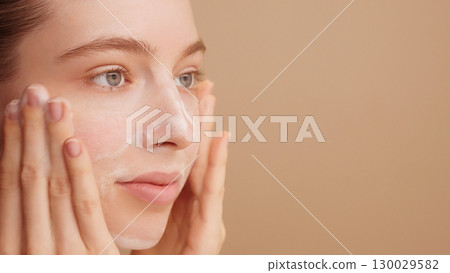 Close-up of a beautiful female face. Woman applying cleansing foam gently washing face ads. Bubbles. Copy space. Beauty daily routine. Skincare treatment. Selfcare. Commercial shoot. Beige Background Close-up of a beautiful female face. Woman applying cleansing foam gently washing face ads. Bubbles. Copy space. Beauty daily routine. Skincare treatment. Selfcare. Commercial shoot. Beige Background 130029582