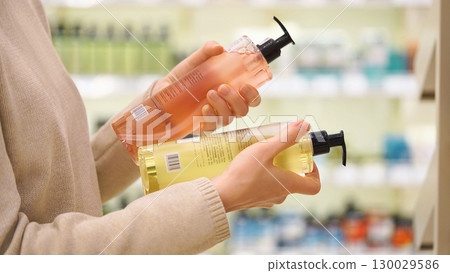 Customer compares haircare, personal care, skincare products in a cosmetics aisle. Woman reads labels and examines the ingredients. Closeup female hands holds two different bottles. Conscious choice. Customer compares haircare, personal care, skincare products in a cosmetics aisle. Woman reads labels and examines the ingredients. Closeup female hands holds two different bottles. Conscious choice. 130029586