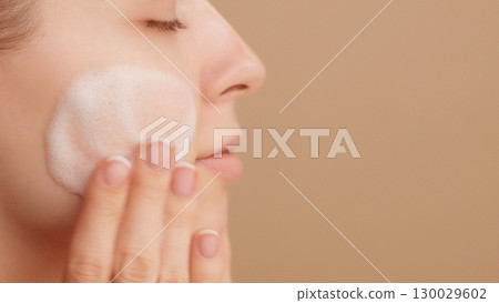 Close-up of a beautiful female face. Woman applying cleansing foam gently washing face ads. Bubbles. Beauty daily routine. Commercial shoot. Skincare treatment. Selfcare. Copy space. Beige Background Close-up of a beautiful female face. Woman applying cleansing foam gently washing face ads. Bubbles. Beauty daily routine. Commercial shoot. Skincare treatment. Selfcare. Copy space. Beige Background 130029602