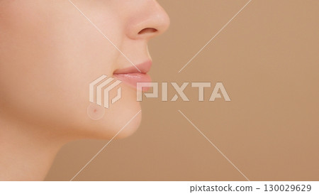 Close-up of a young woman applies a round acne patch to a blemish for spot treatment. Acne treatment, zit patch, acne spot patch ads. Young girl and smile in studio on beige background. Copy space 130029629