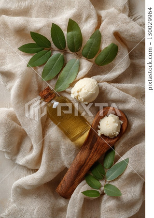 Natural Ingredients: Raw Shea Butter, Oil, Wooden Scoop, Green Leaves on Neutral Cloth 130029964