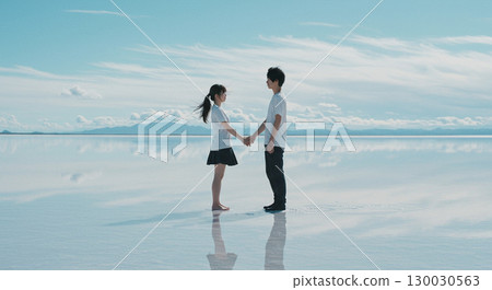 Two people holding hands in a salt lake that reflects like a mirror 130030563