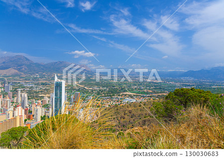Aerial panoramic view of Benidorm city with skyscrapers hotel buildings, La Nucia Hills valley and Puig Campana mountain Sierra Cortina in summer day, Valencian Community, Spain 130030683