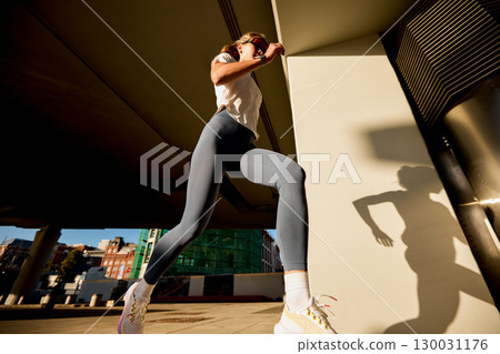 Athletic woman running outdoors in urban scenery during golden hour 130031176