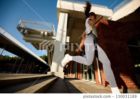 Athletic woman running outdoors in modern urban city environment during the day Athletic woman running outdoors in modern urban city environment during the day 130031189