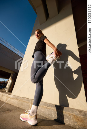 Woman stretching leg during outdoor workout in urban environment Woman stretching leg during outdoor workout in urban environment 130031212