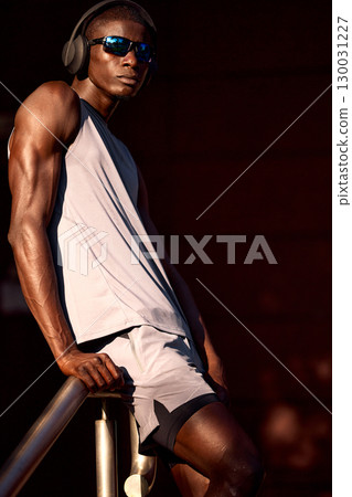 Athletic man outdoors wearing headphones and sunglasses in sporty attire Athletic man outdoors wearing headphones and sunglasses in sporty attire 130031227