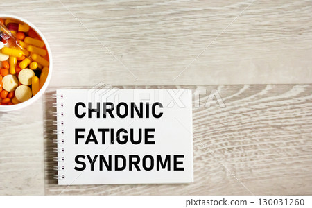 The symbol Chronic Fatigue syndrome on the notebook. White background with pills.  130031260