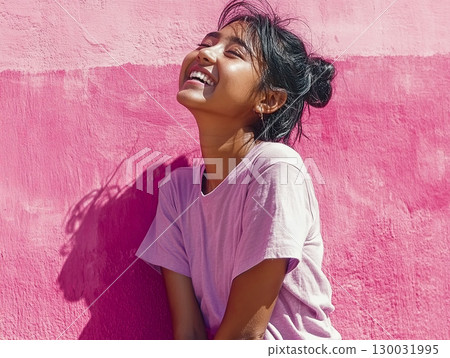Joyful young woman smiling brightly against a vibrant pink wall 130031995