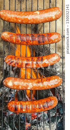 Grilled sausages sizzling on barbecue grill with flames 130032141