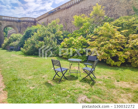 Cozy outdoor seating area with two chairs and a table surrounded by lush greenery and vibrant foliage in a tranquil garden setting 130032272
