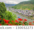 Scenic river view with colorful flowers in foreground, showcasing charming village along the water and lush green hills in the background 130032273