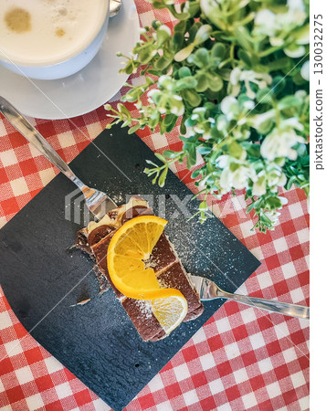Delicious dessert featuring chocolate layers and fresh lemon slices served on a slate plate with a coffee cup and greenery in the background 130032275