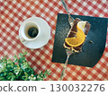 Delicious dessert featuring chocolate cake topped with fresh orange slices, served alongside a cup of espresso on a checkered tablecloth 130032276