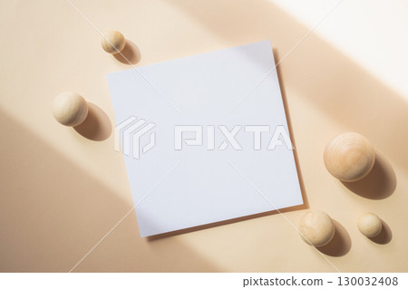 Empty white blank greeting or invitation card with wooden ball on beige background. Mock up presentation. 130032408