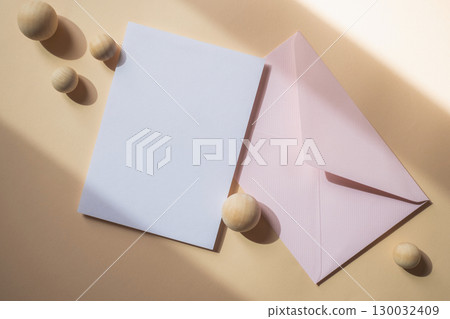 Empty white blank greeting or invitation card with pink envelope on beige background. Mock up presentation. 130032409
