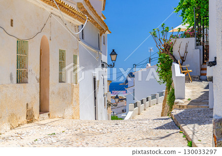 Altea old town narrow empty street with typical white houses traditional buildings in sunny summer day, Altea city historical centre Casco Antiguo, Alicante province, Valencian Community, Spain 130033297
