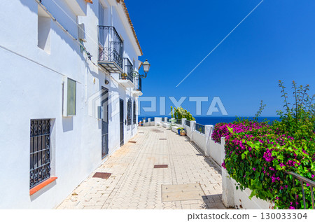 Altea old town narrow street with typical white houses buildings, Altea bay Mediterranean Sea water in sunny summer day, Altea city historical centre, Alicante province, Valencian Community, Spain 130033304