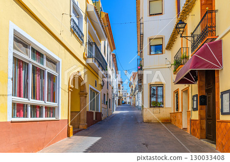 Old town Calpe city historical centre narrow street with typical houses colorful traditional buildings in sunny summer day, Calp Casco Antiguo, province of Alicante, Valencian Community, Spain Old town Calpe city historical centre narrow street with typical houses colorful traditional buildings in sunny summer day, Calp Casco Antiguo, province of Alicante, Valencian Community, Spain 130033408