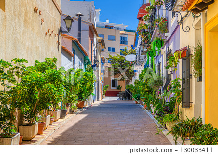 Old town Calpe city historical centre narrow street with typical houses colorful traditional buildings, plants in pots in sunny summer day, Calp Casco Antiguo, Valencian Community, Spain 130033411