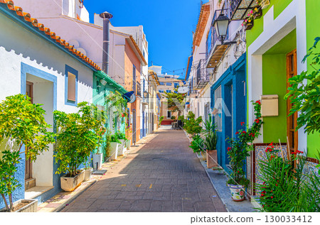 Old town Calpe city historic centre narrow street with typical houses colorful traditional buildings multicolored walls, plants in pots in sunny day, Calp Casco Antiguo, province of Alicante, Spain Old town Calpe city historic centre narrow street with typical houses colorful traditional buildings multicolored walls, plants in pots in sunny day, Calp Casco Antiguo, province of Alicante, Spain 130033412