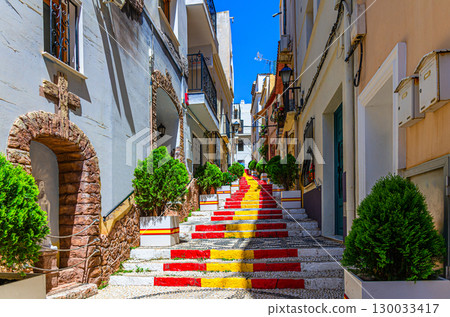 Spanish Steps Spanish flag stairs staircase narrow pedestrian Calle Puchalt street, colorful typical buildings houses in old town Calpe city historical centre in sunny day, Valencian Community, Spain 130033417