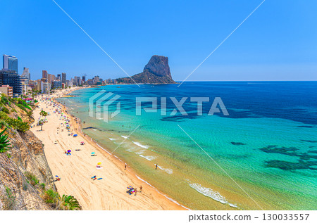 Calpe town coastline aerial view panorama Costa Blanca coast with Penyal d'Ifac rock mountain, sandy beach, Calpe bay Mediterranean Sea with azure water in sunny summer day, Alicante province, Spain 130033557
