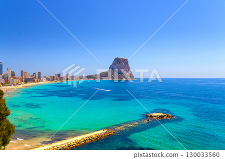 Calpe town coastline aerial view panorama Costa Blanca coast with rock mountain Penon de Ifach, sandy beach, Calpe bay Mediterranean Sea with azure turquoise water in sunny summer day, Spain 130033560